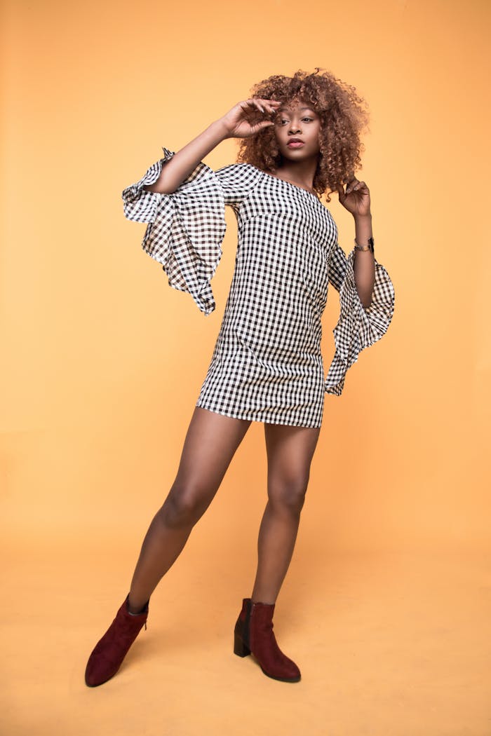 Stylish young woman posing in a modern checkered dress against a vibrant orange backdrop.